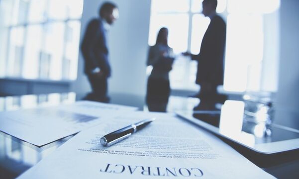 Contract to sign Close-up of business contract with pen at workplace on background of office workers interacting